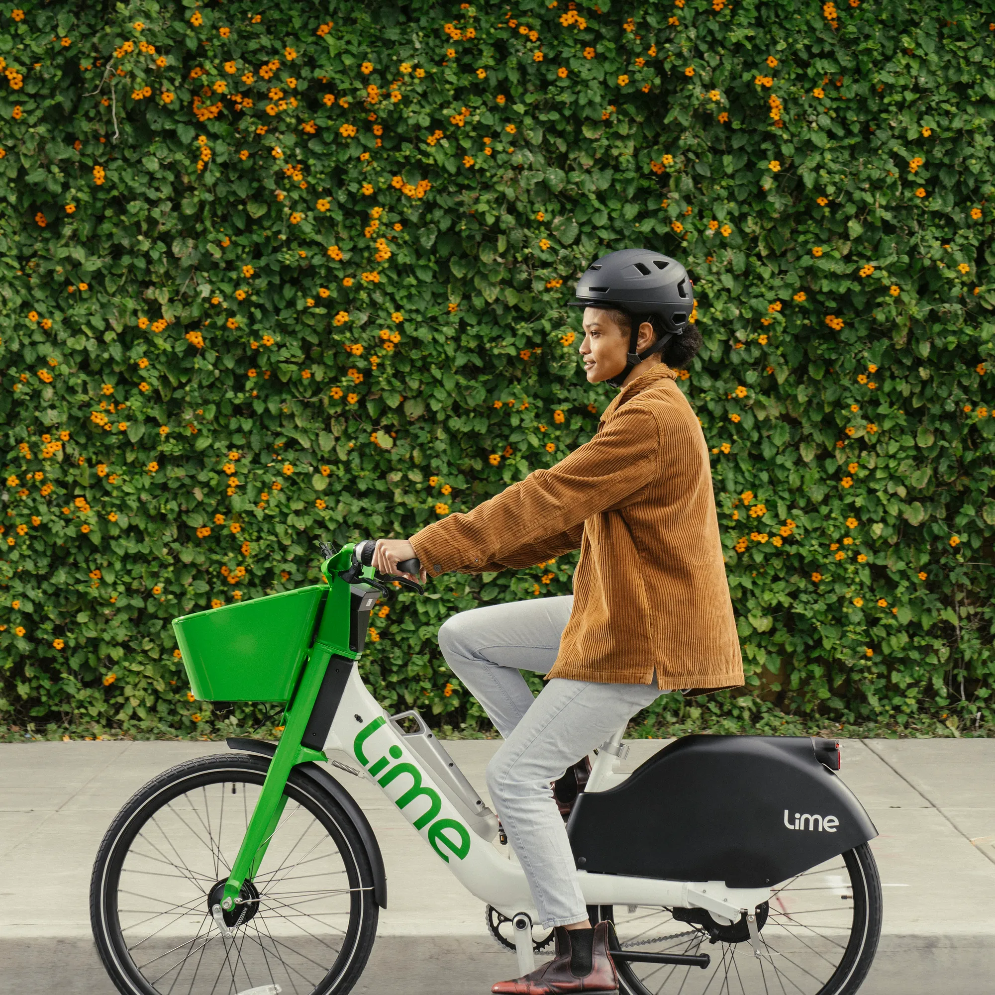 Helmeted rider on a Lime electric bike beside a leafy wall